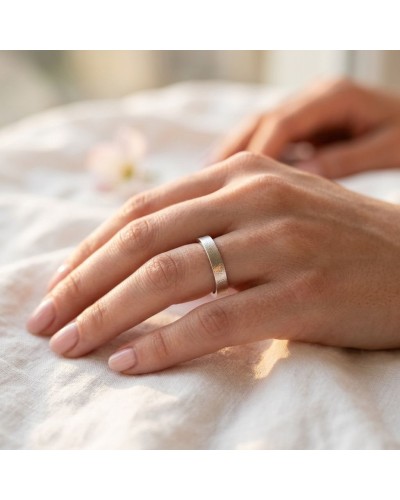 Alliance SABLE 4 mm Femme en or: doigt avec bague dorée et argentée, peau nude, fond doux et éclairage chaud.