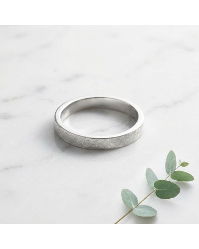 Alliance SABLE 4 mm Homme en or: bague argentée à finition satinée, motif texturé, reposant sur marbre avec feuille verte.