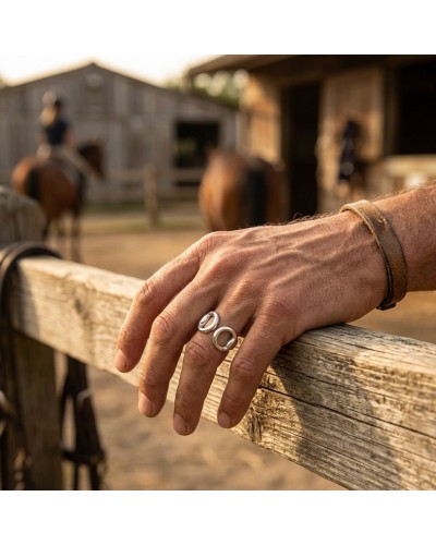 Bague MORS homme en argent rhodié portée sur le doigt, devant une clôture en bois et un décor rural.