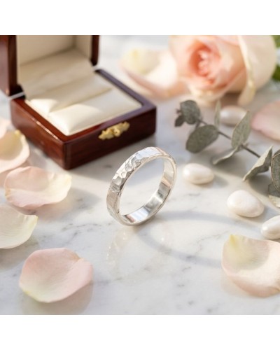 Alliance FRAGMENT 4 mm Femme en or : alliance argentée façonnée, posé près d’un coffret en bois et de petals sur marbre.