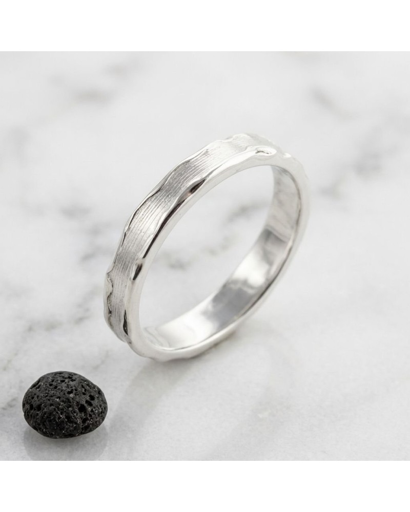 Alliance LAVE 4 mm homme en or: bague argentée oxydée motif ondulé, posée sur pierre noire et marbre.