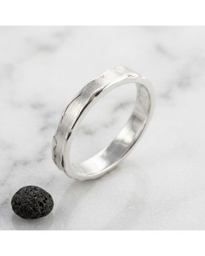 Alliance LAVE 4 mm homme en or: bague argentée oxydée motif ondulé, posée sur pierre noire et marbre.