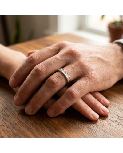 Alliance LAVE 4 mm homme en or: homme porte alliance argentée avec texture martelée sur anneau épais posé sur une table en bois.