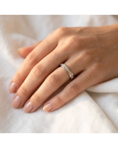 Alliance féminine en or avec pierres 4 mm, prise au doigt sur une main posée sur tissu blanc.