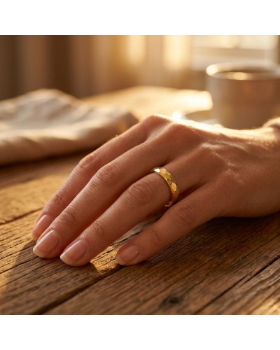 Alliance FLASH 4 mm femme en or: doigt portant une bague dorée à motif facettes sur table en bois, lumière chaude.