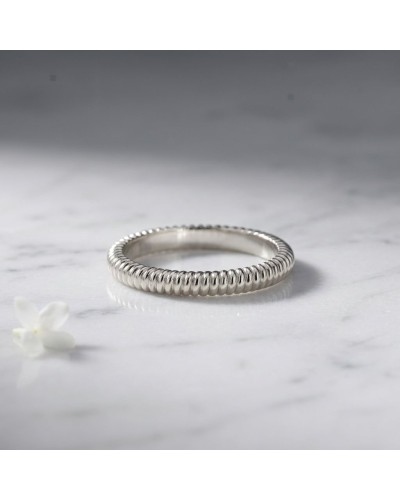 Alliance ELEKTRA 3 mm femme en or: bague fine argentée avec motif torsadé posée sur marbre, fleur blanche à côté.