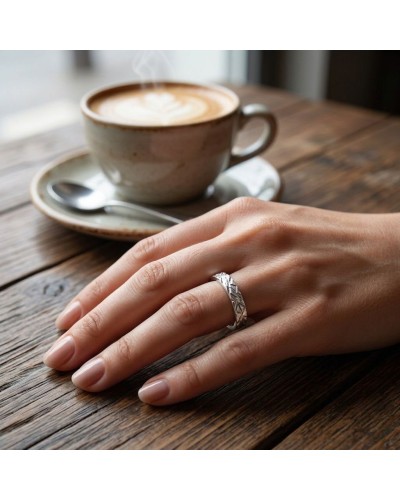 Alliance ECORCE 4 mm Femme en or: main féminine portant une bague argentée à motif géométrique, café sur table en bois.