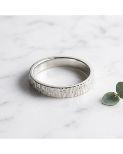 Alliance GOUTTE 4 mm Homme en or: alliance argentée à texture martelée, posé sur marbre avec petite feuille verte.