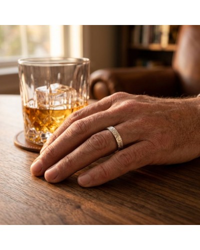 Alliance GOUTTE 4 mm Homme en or: doigt masculin portant une bague argentée sur fond de verre de whisky et bois.