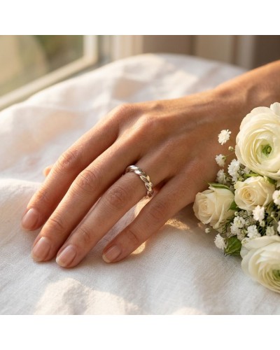 Alliance THOR torsadée 4 mm en or sur le doigt d’une main féminine, près d’un bouquet de roses blanches.