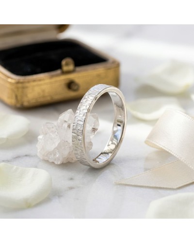 Alliance GOUTTE 4 mm Femme en or: bague argenté avec motif texturé, posée près de cristaux et d’un petit coffret doré, sur ruban