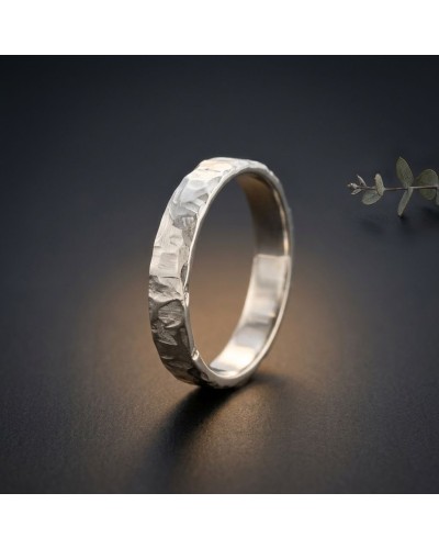 Alliance FRAGMENT 4 mm Homme en or: bague argentée à texture sculptée sur fond sombre, légère lumière chauffante.