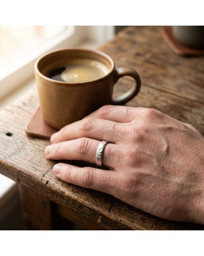Alliance FRAGMENT 4 mm Homme en or: main masculine posée sur une table en bois, doigt portant une bague argentée texturée près d