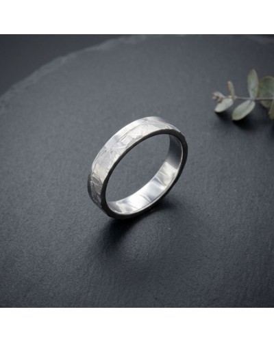 Alliance homme en or gris 4 mm avec fini martelé, posé sur fond sombre.