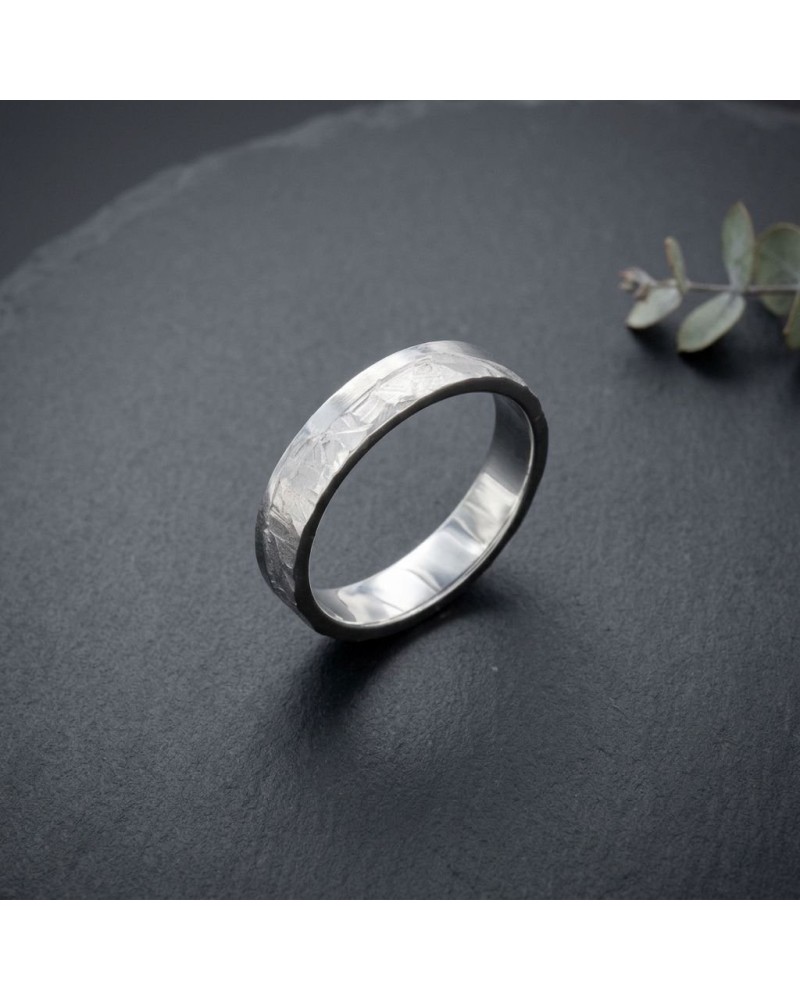 Alliance homme en or gris 4 mm avec fini martelé, posé sur fond sombre.