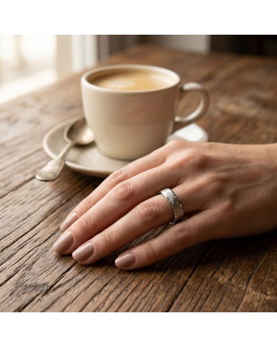 Alliance FUSION 4 mm Femme en or: doigt portant un anneau argenté texturé posé sur une table en bois avec tasse de café.