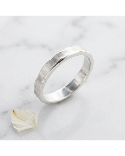 Alliance femme en or blanc 4 mm à fini texturé, bague simple posée sur marbre avec pétale.