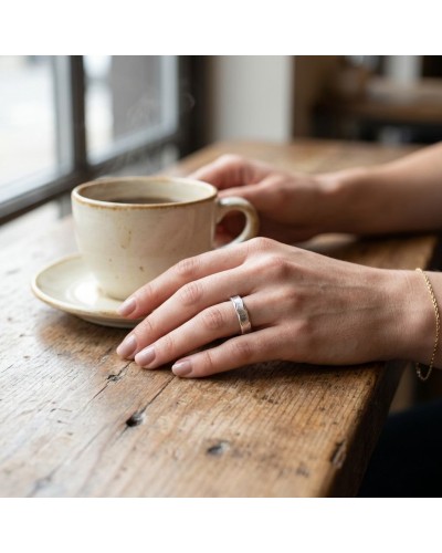 Alliance LAVE 4 mm femme en or : main féminine portant une bague argentée sur une table en bois près d’une tasse de café.