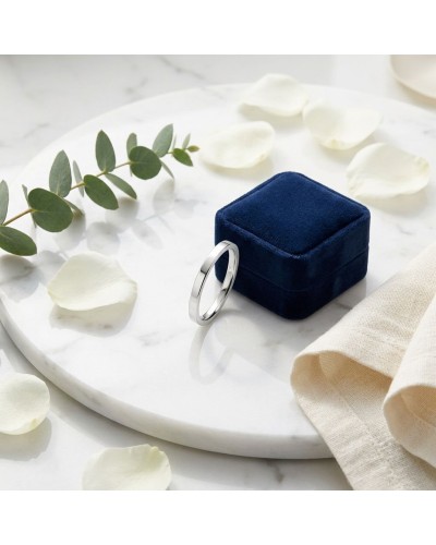 Alliance MATRIX lisse 2 mm homme en or - bague argentée posée à côté d’un écrin bleu sur piédestal marbré, pétales et feuillage