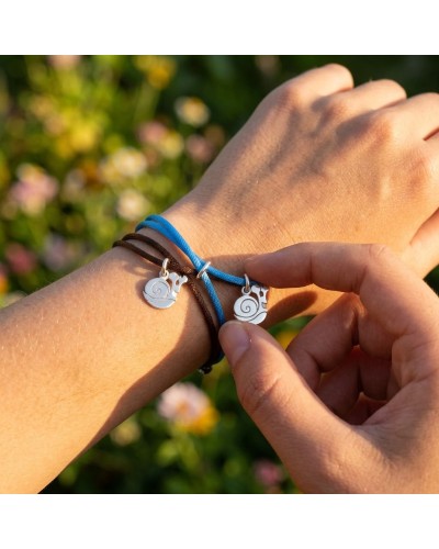 Bracelets assortis portant des breloques escargots argentées, noués autour du poignet avec des cordons bleu et brun, fond jardin