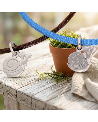 Bracelets à cordon bleu et marron avec pendentifs en forme de coquille d’escargot argentée, posés près d’un petit pots et de mou