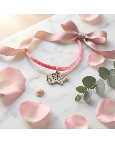 Bracelet BB TORTUE sur cordon rose, gravure tortue argentée ornement simple, posé sur marbre avec pétales et coquillages.