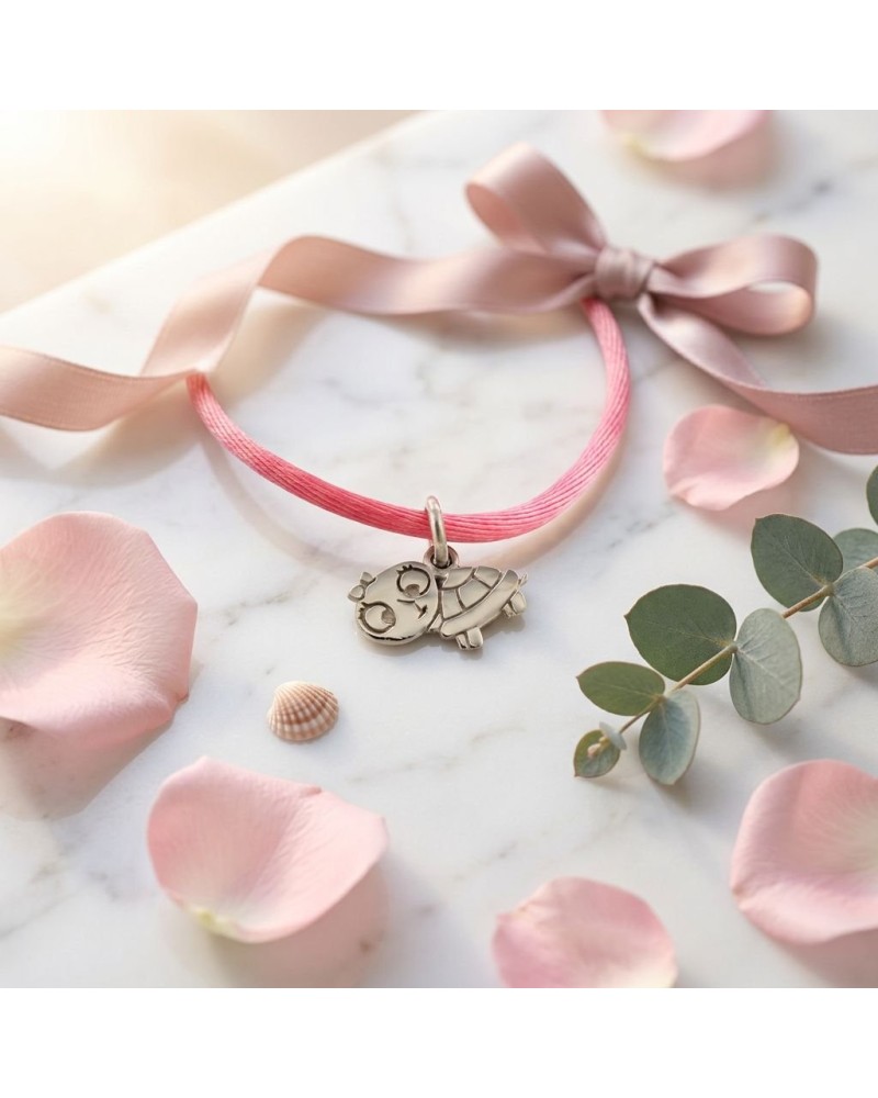 Bracelet BB TORTUE sur cordon rose, gravure tortue argentée ornement simple, posé sur marbre avec pétales et coquillages.