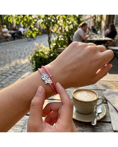 Bracelet BB TORTUE en corde rose autour du poignet, petit pendentif tortue argenté, scène de café en arrière-plan.
