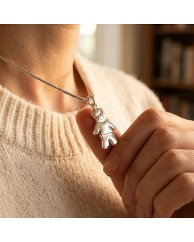 Pendentif ADAM en forme d'homme argenté porté sur une chaîne, tenu entre les doigts.