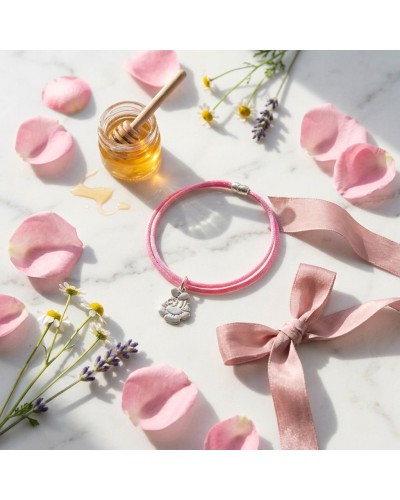 Bracelet BB ABEILLE rose en cordon, avec pendentif coccinelle sur fond floral pastel et ruban rose clair à côté.