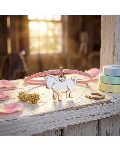 Bracelet BB PONEY avec pendentif en forme de poney blanc sur cordon rose, posé sur surface en bois avec rubans colorés à l’arriè