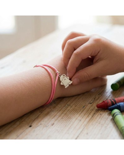Bracelet enfant rose avec pendentif forme demi-figurine, porté au poignet; crayons pastels sur une table en bois. Bracelet BB UN