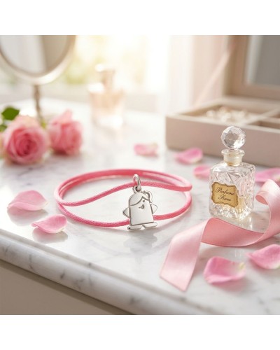Bracelet élastique rose avec pendentif mascotte blanche, posé sur une surface marble, près d’un flacon de parfum et de roses déc