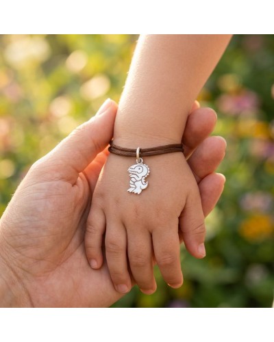 Bracelet en cuir marron avec pendentif dinosaure argenté sur poignet d’enfant, mains liées. Bracelet BB DINO.
