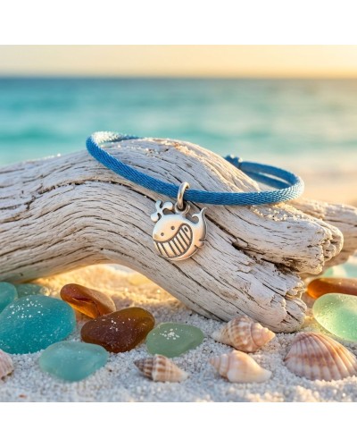 Bracelet bleu en cordon avec pendentif fantaisie en forme de baleine souriante sur bois flotté, plage et coquillages au soleil.