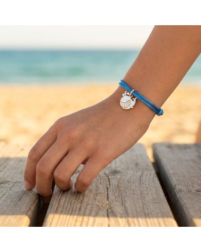 Bracelet bleu en cordon autour du poignet avec charmante breloque baleine, sur fond plage et mer. Bracelet BB BALEINE.