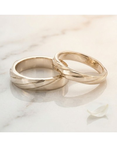 Alliance ENTRELACE Femme en or: deux bagues d’or entrelacées posées sur une surface claire, pétales blancs à proximité.