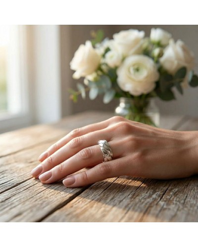Alliance Femme en or à motif torsadé portée sur le dos de la main féminine, bouquet blanc flou en arrière-plan.
