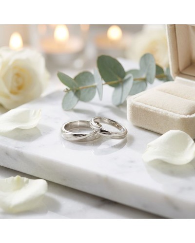 Alliances féminines en argent sur un socle marbré, entourées de pétales et d’une boîte à bijoux beige, ambiance romantique. Alli