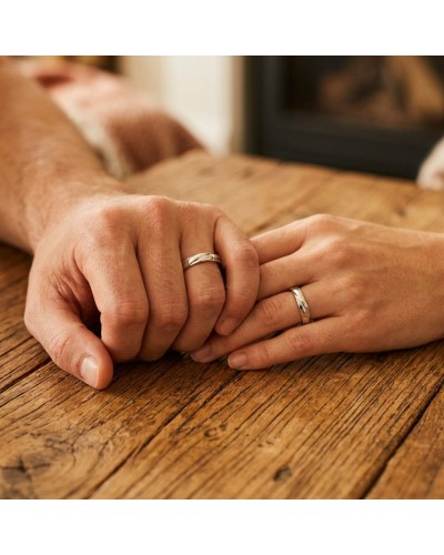 Alliance de mains entre un homme et une autre personne, bagues argentées sur doigts, posé sur une table en bois.