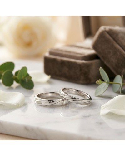 Alliance homme en or argenté posées sur marbre, avec pétales et évasions de fleurs, symboles de mariage.