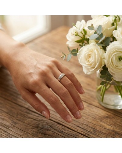 Alliance Entrelaçée femme en or sur doigt, près d’un bouquet de roses blanches sur une table en bois.