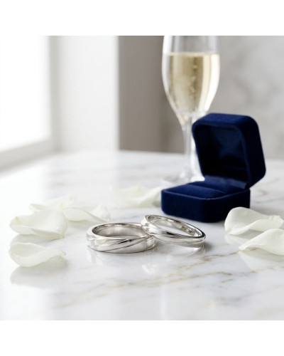 Alliance hommes en or blanc argenté, bagues entrecroisées près d’un coffret bleu et d’un verre de champagne sur marbre.