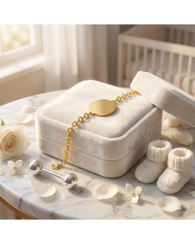 Bracelet en maille dorée Or jaune 18k posé sur un élégant écrin grisIts Providence; chaussons bébé blancs et fleurs sur table en