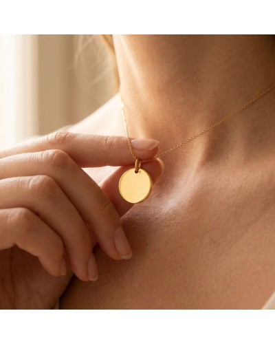 Médaille ronde en or jaune 18k sur chaîne délicate, portée près du collier sur le cou.