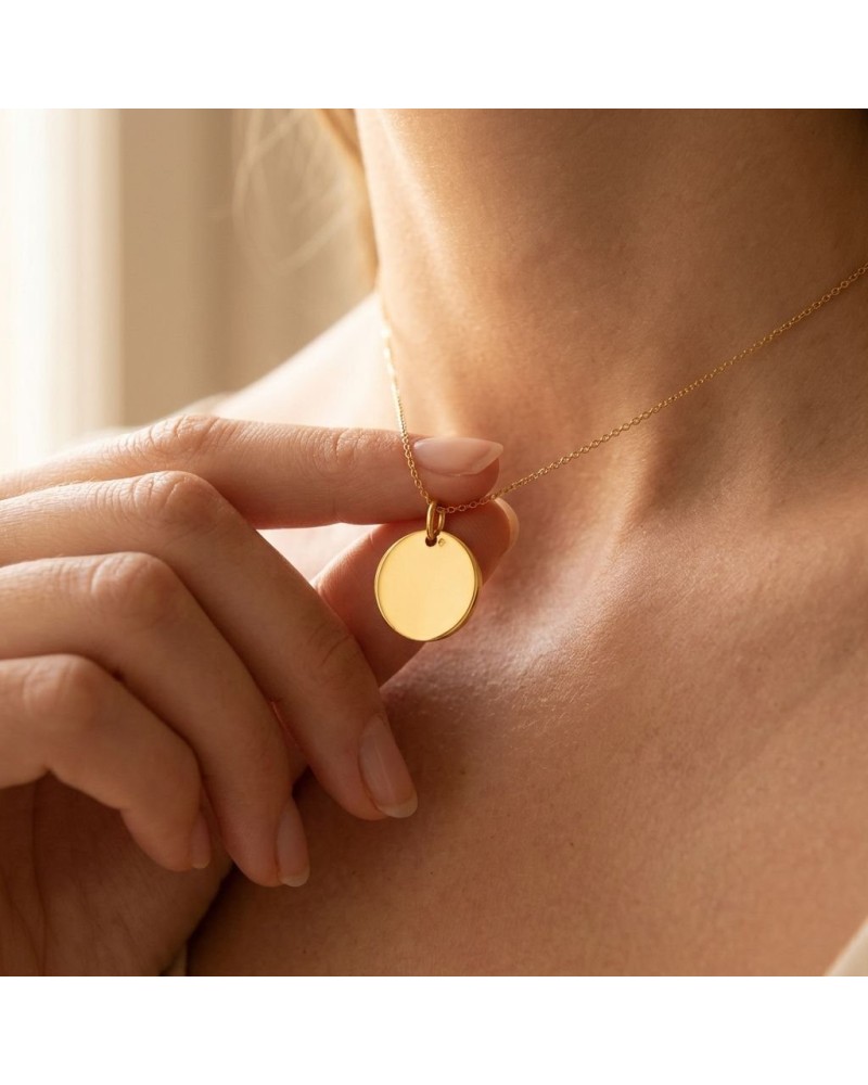 Médaille ronde en or jaune 18k sur chaîne délicate, portée près du collier sur le cou.