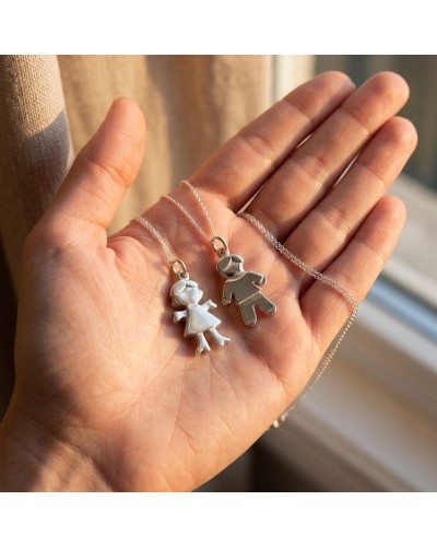 Pendentifs EVE en forme de petits personnages féminin et masculin sur chaîne argentée, présentés dans la paume.
