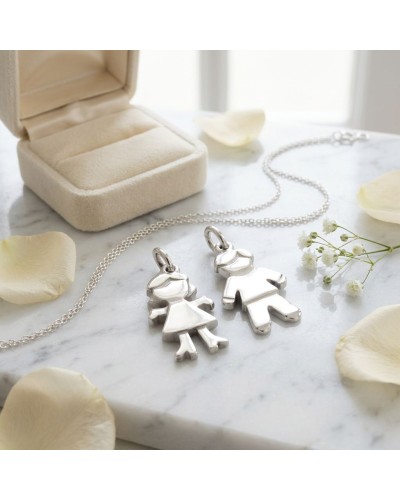 Pendentifs EVE en forme d’enfant fille et garçon en argent sur chaîne, posés sur marbre près d’un écrin.