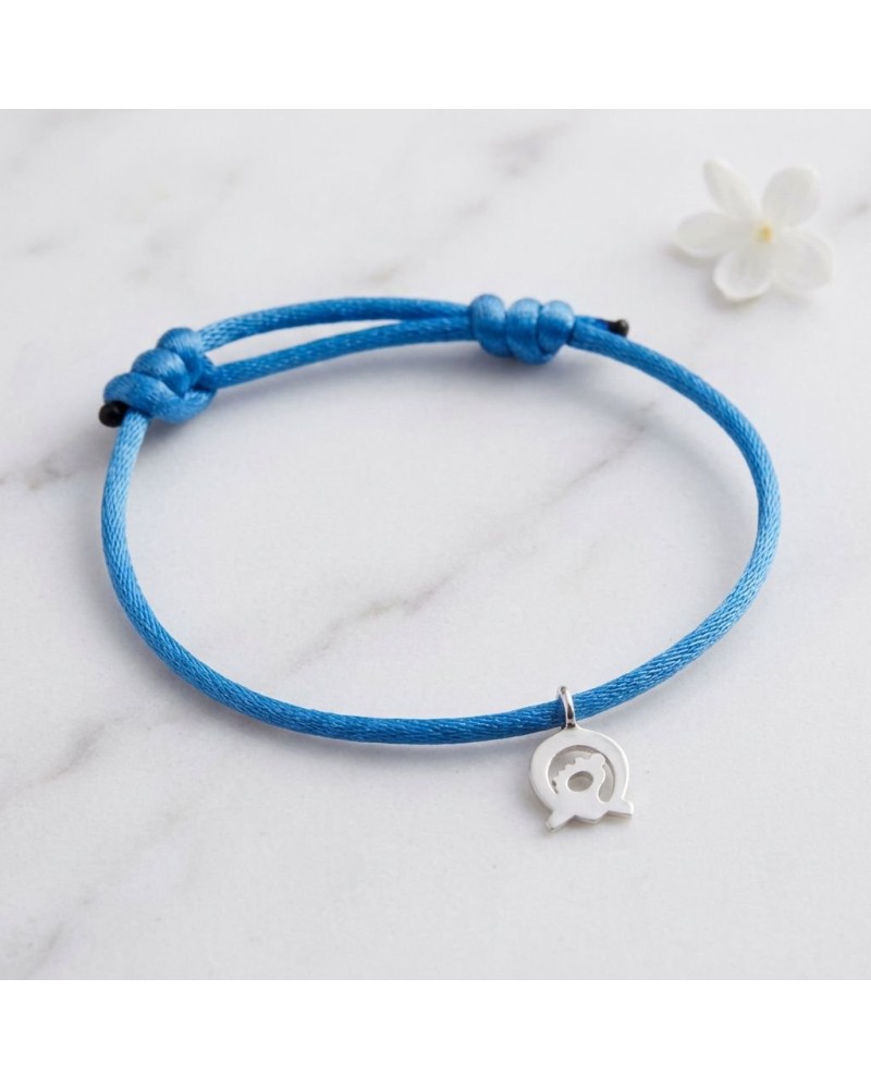 Bracelet bleu en cordon avec petit pendentif argenté en forme d’élément central, posé sur marbre. Bracelet CONNEXION Murial sout