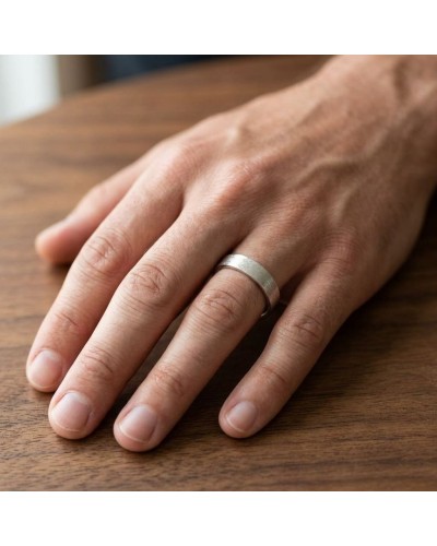 Alliance homme en or brossé sur doigt posé sur une table en bois, style minimaliste.
